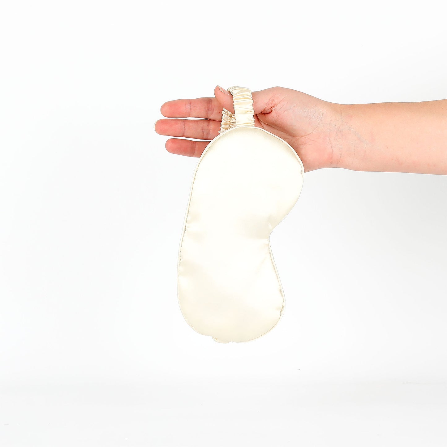 Hand holding a satin eye mask on a white background