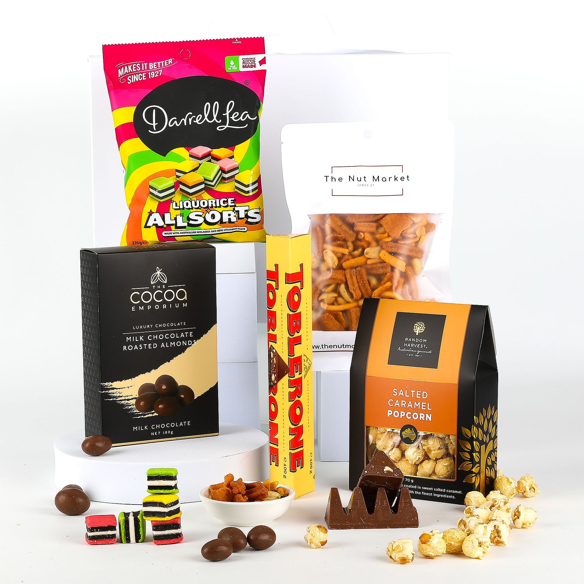 Assorted snacks including Darrell Lea Licorice Allsorts, salted caramel popcorn & Toblerone chocolate on a white background.