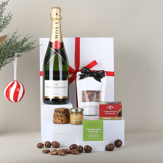Gift set with a bottle of Chandon champagne, caramelised popcorn, and other treats on a light background.