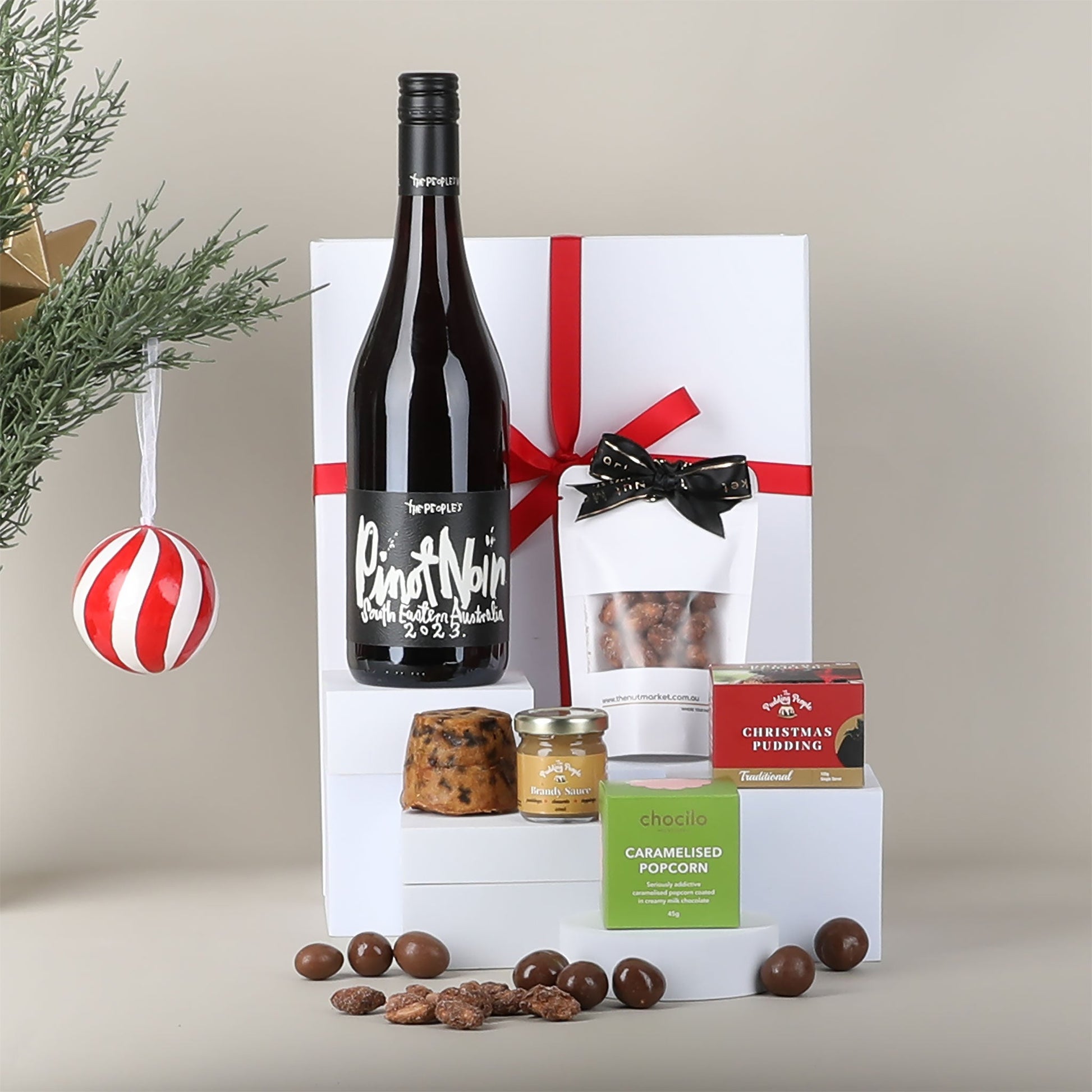 Gift set with a bottle of wine, pudding, caramelised popcorn and other treats on a neutral background