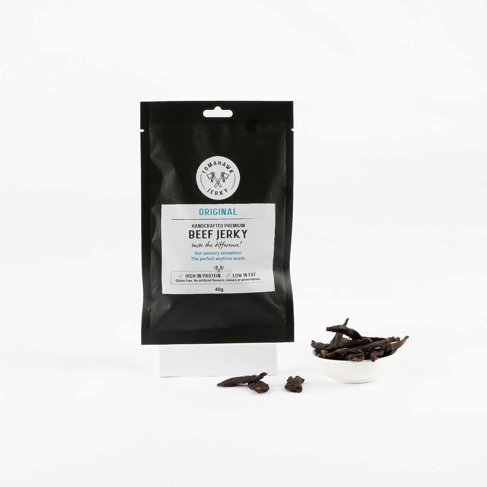 Black package of Original Handcrafted Premium Beef Jerky with beef jerky pieces on a white background